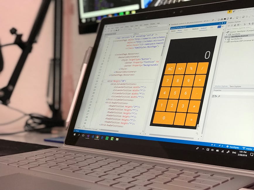 A person using a laptop computer placed on a dark surface, with hands actively typing on the keyboard. The laptop screen displays a software development environment, showing lines of code in multiple 